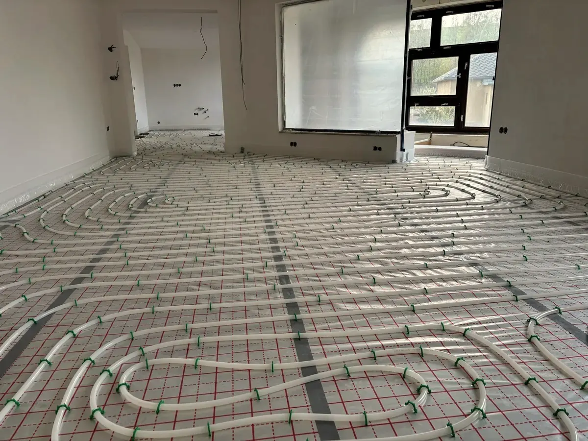 Empty room whose floor is covered in foil-faced sheets with taped seams, underfloor heating pipes clipped on top