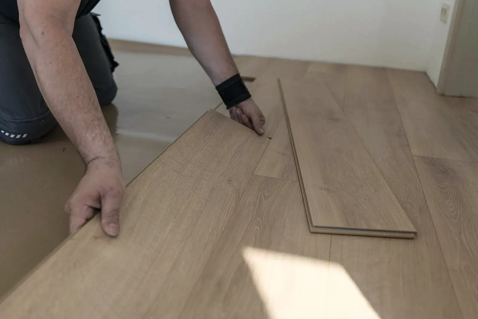 A fitter kneels on the underlayment and angles a laminate plank into the previous row