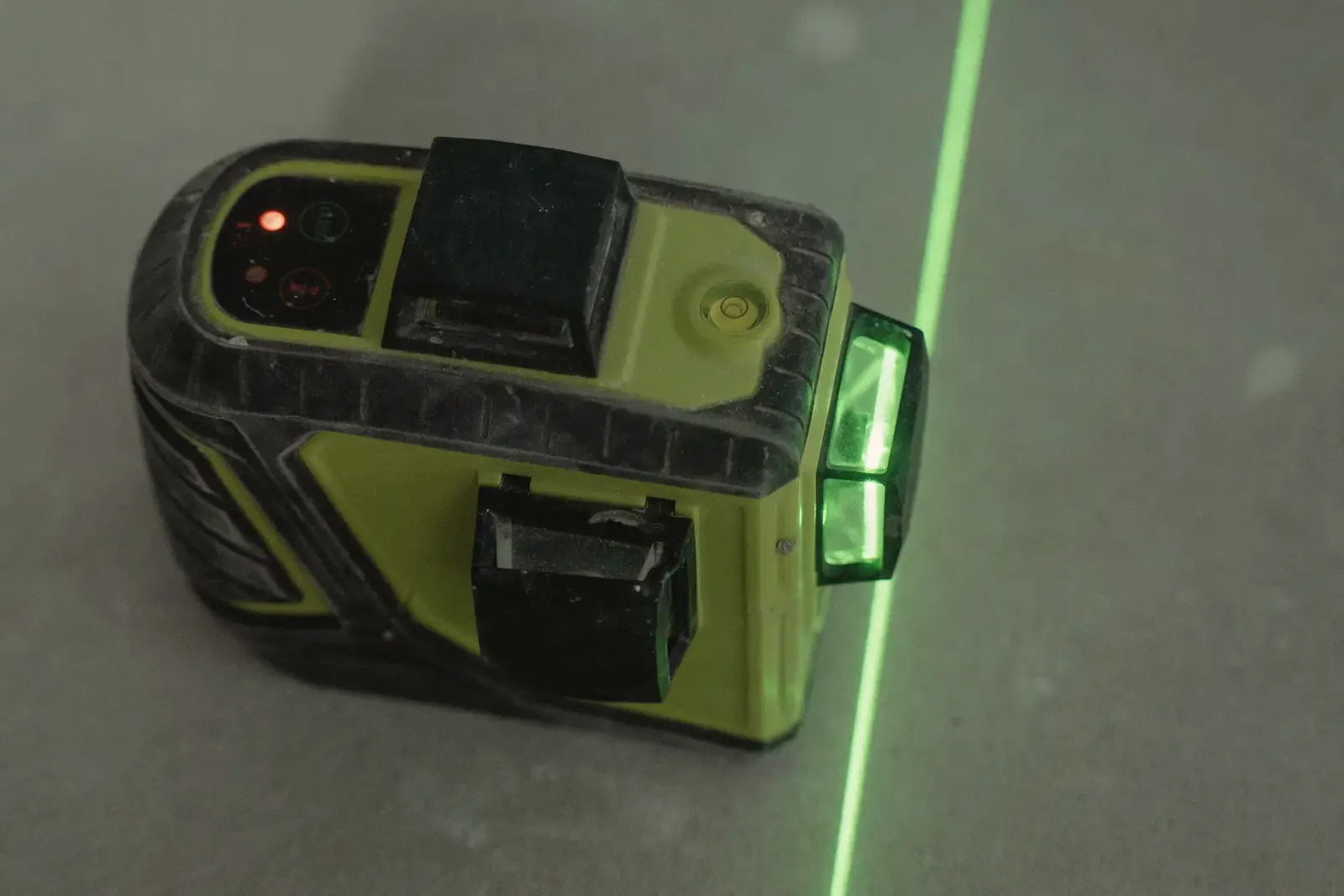 A line laser projects a straight green line across a bare concrete floor