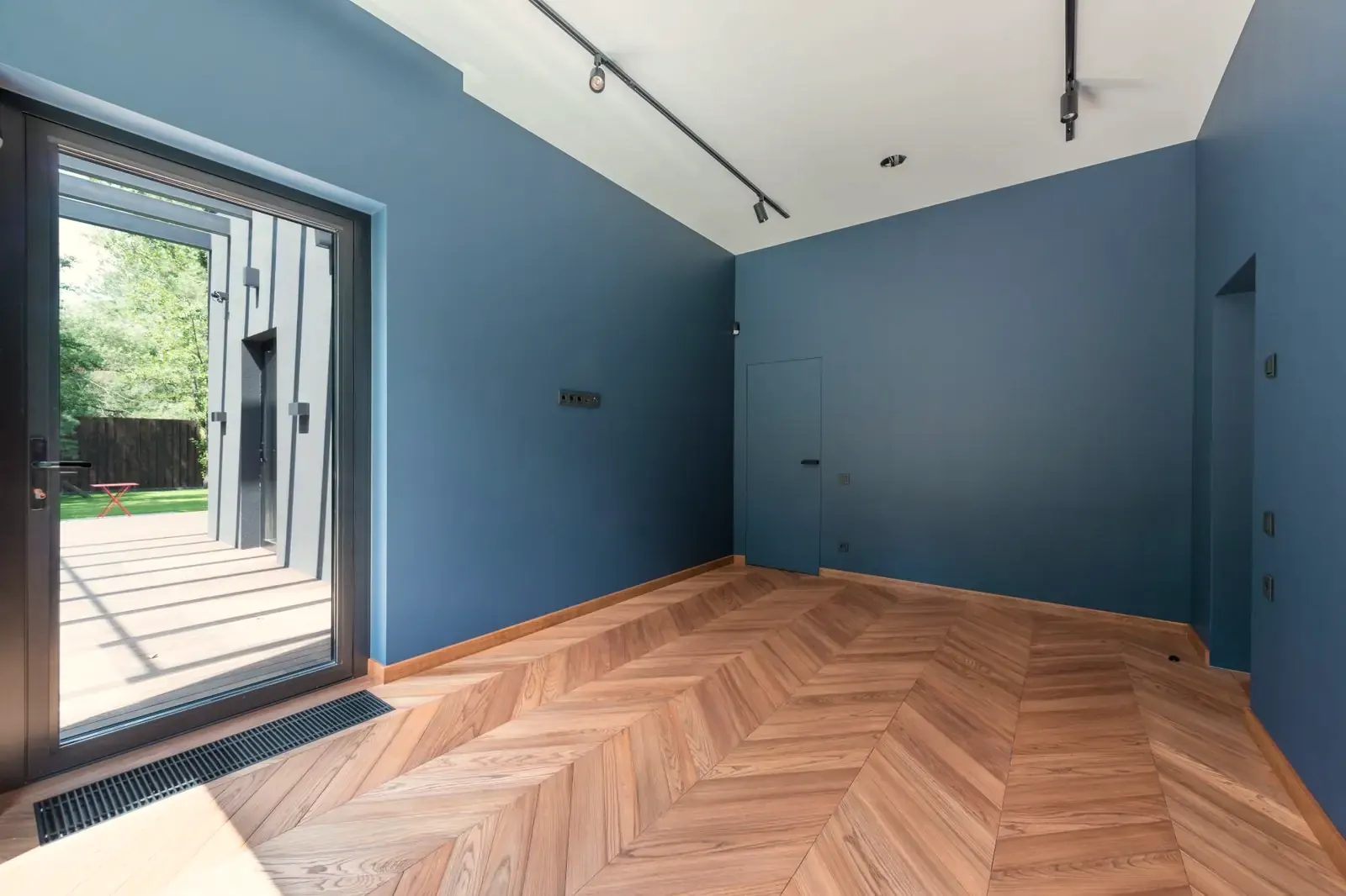 A finished empty room with blue walls and an even chevron oak floor, ready to be furnished