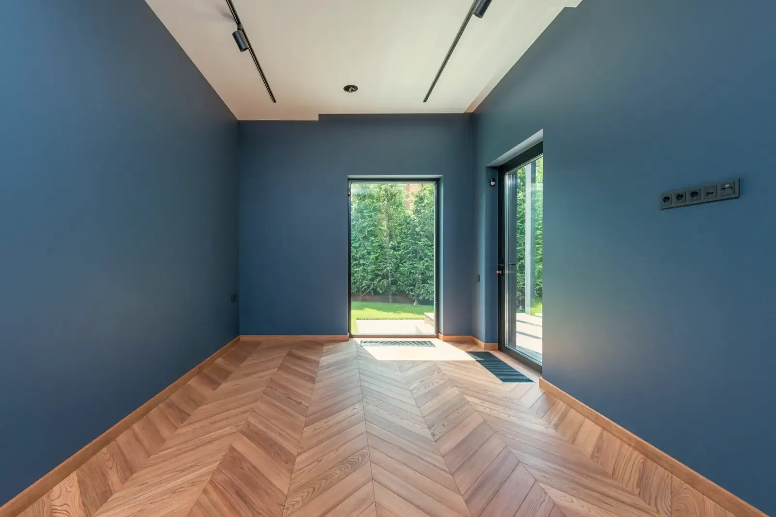 An empty room with blue walls and a newly laid oak floor running up to a glass door
