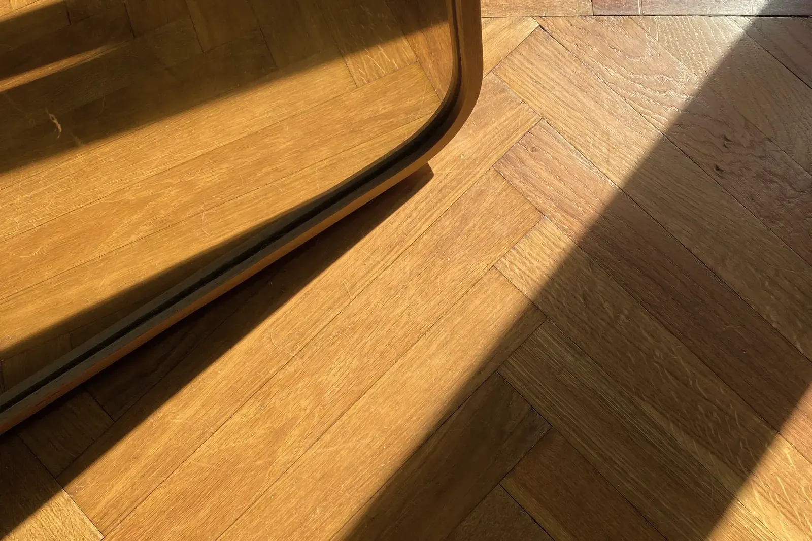 Sunlight across an oak herringbone floor whose border course follows a curved wall base