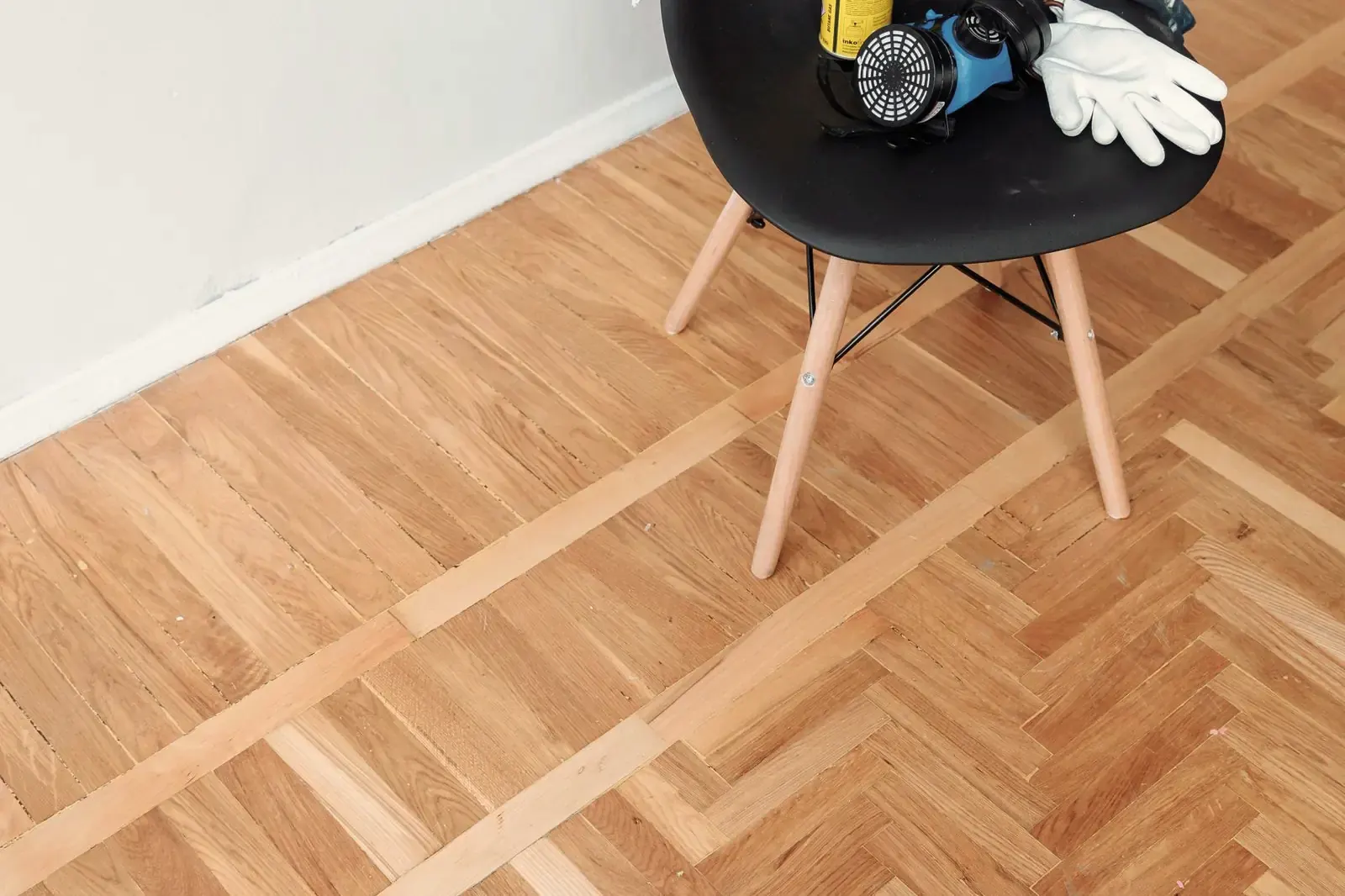 Oak herringbone floor framed by a straight border band, a chair with gloves and a dust mask standing on it