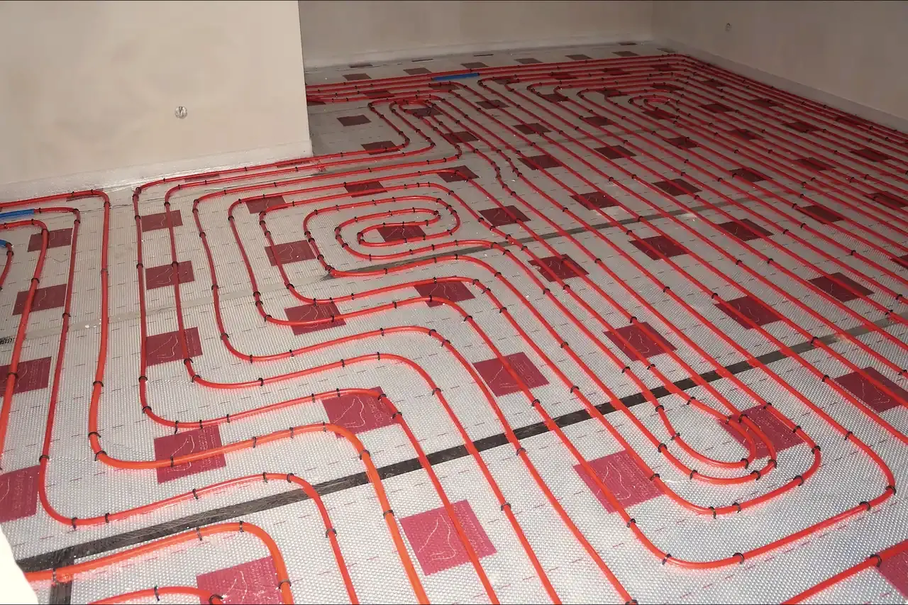 Tubos rojos de suelo radiante fijados en bucles ordenados sobre placas de aislamiento con lámina, a lo largo de una estancia vacía antes de echar la solera