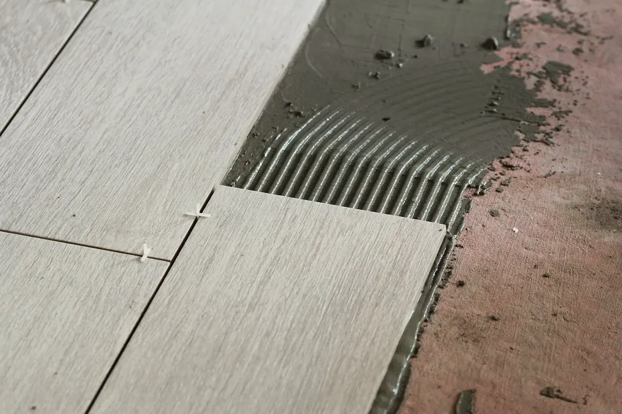 Notched trowel ridges in fresh tile adhesive next to wood-look floor tiles already laid with cross spacers