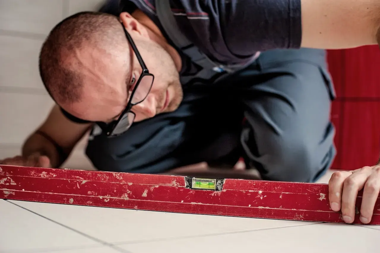 A tiler bends low over the laid floor tiles and checks them with a long bubble level