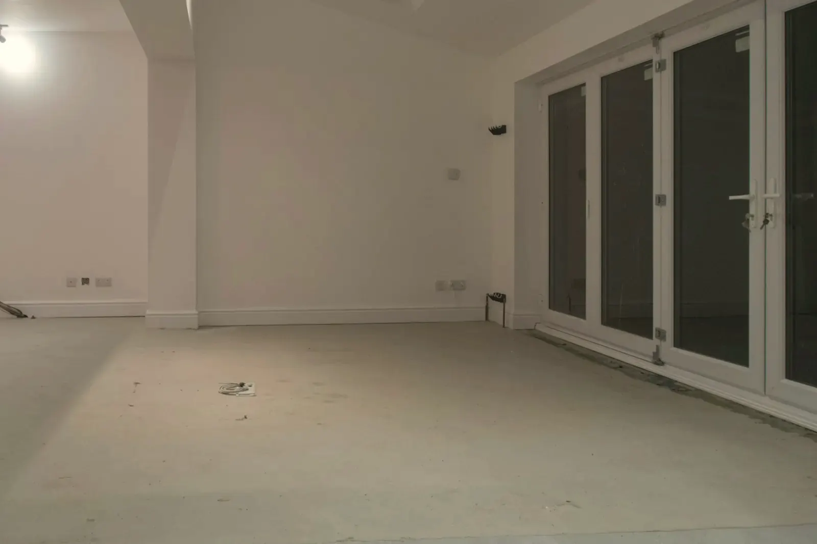 An empty white room with a smooth, clean screed floor ready for the new flooring, next to a row of glass doors