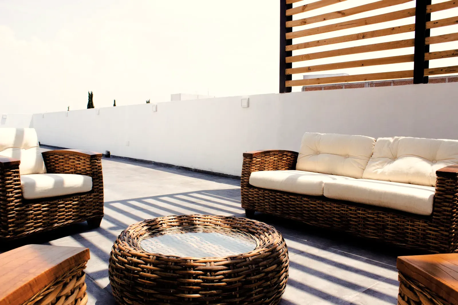 Roof terrace with large gray slabs laid tight to a white parapet wall, wicker sofas and a timber screen