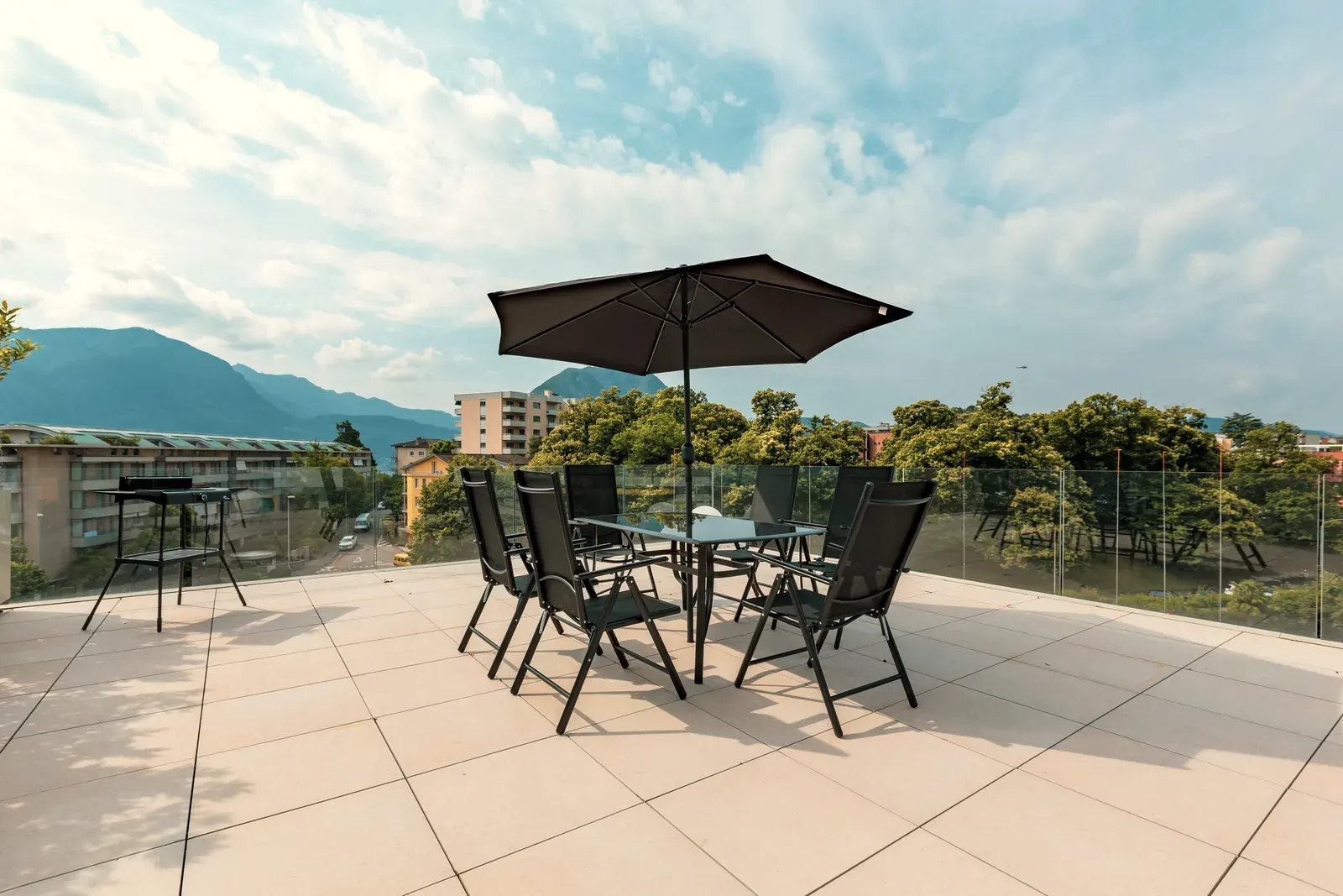 Roof terrace laid with large light porcelain slabs in a straight grid, glass balustrade and mountains behind