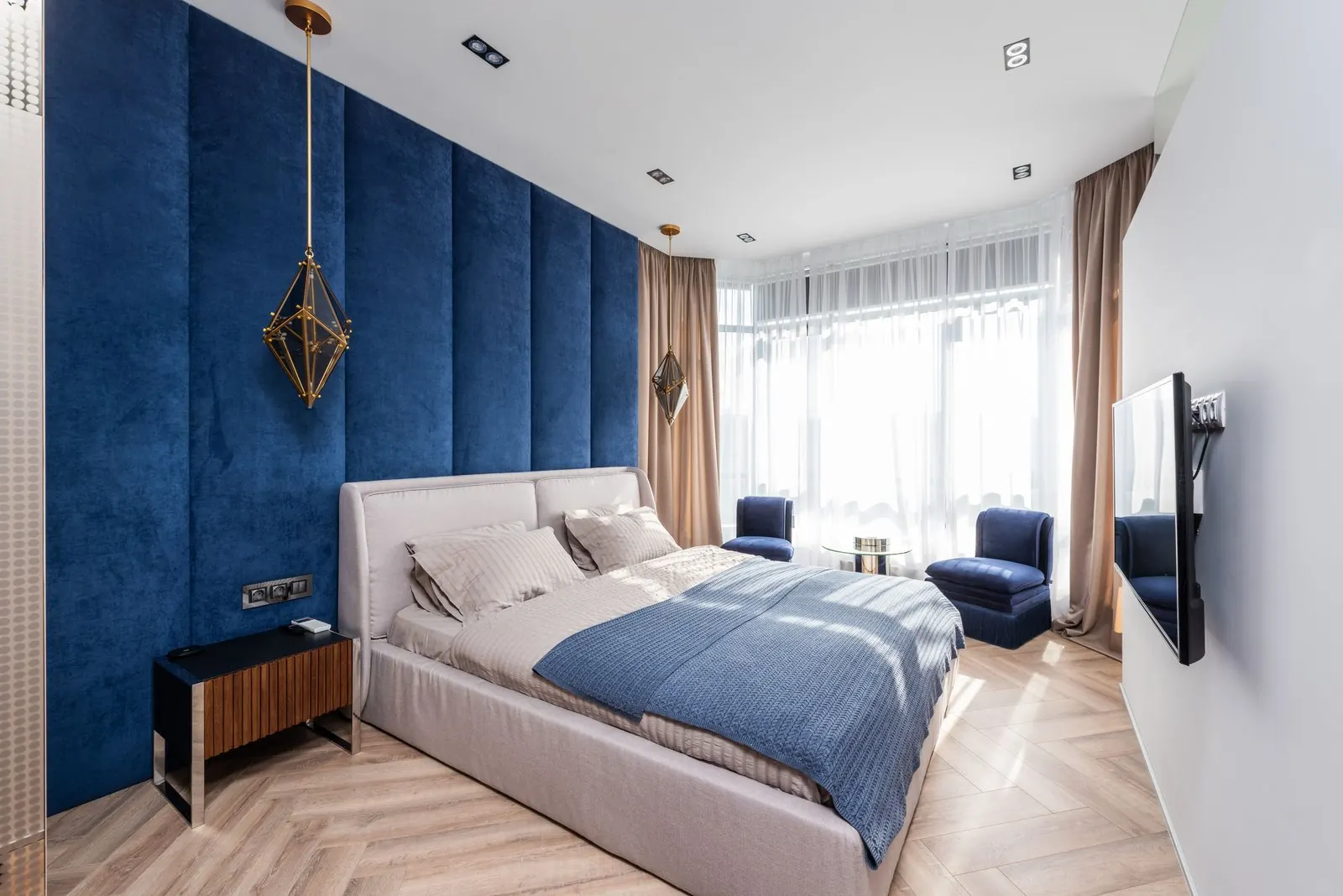 Bedroom with a light oak herringbone floor and blue upholstered wall
