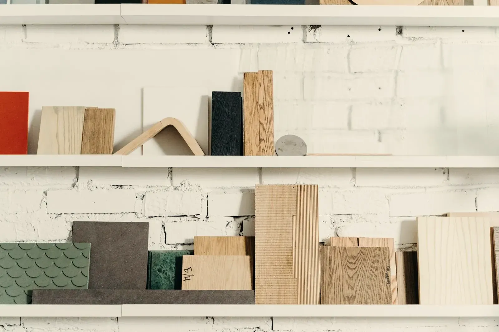 Wood, stone and tile samples lined up on white shelves against a painted brick wall
