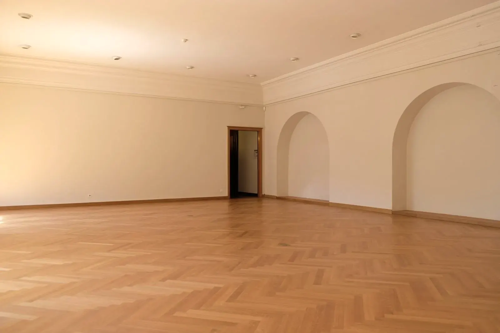 Large empty room with oak herringbone parquet running up to the skirting boards and arched wall niches