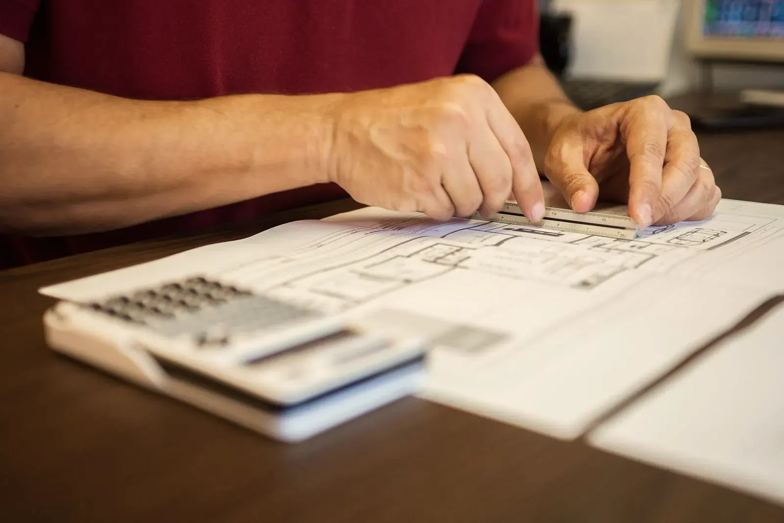 Hands measuring a printed floor plan with a ruler, a calculator beside it