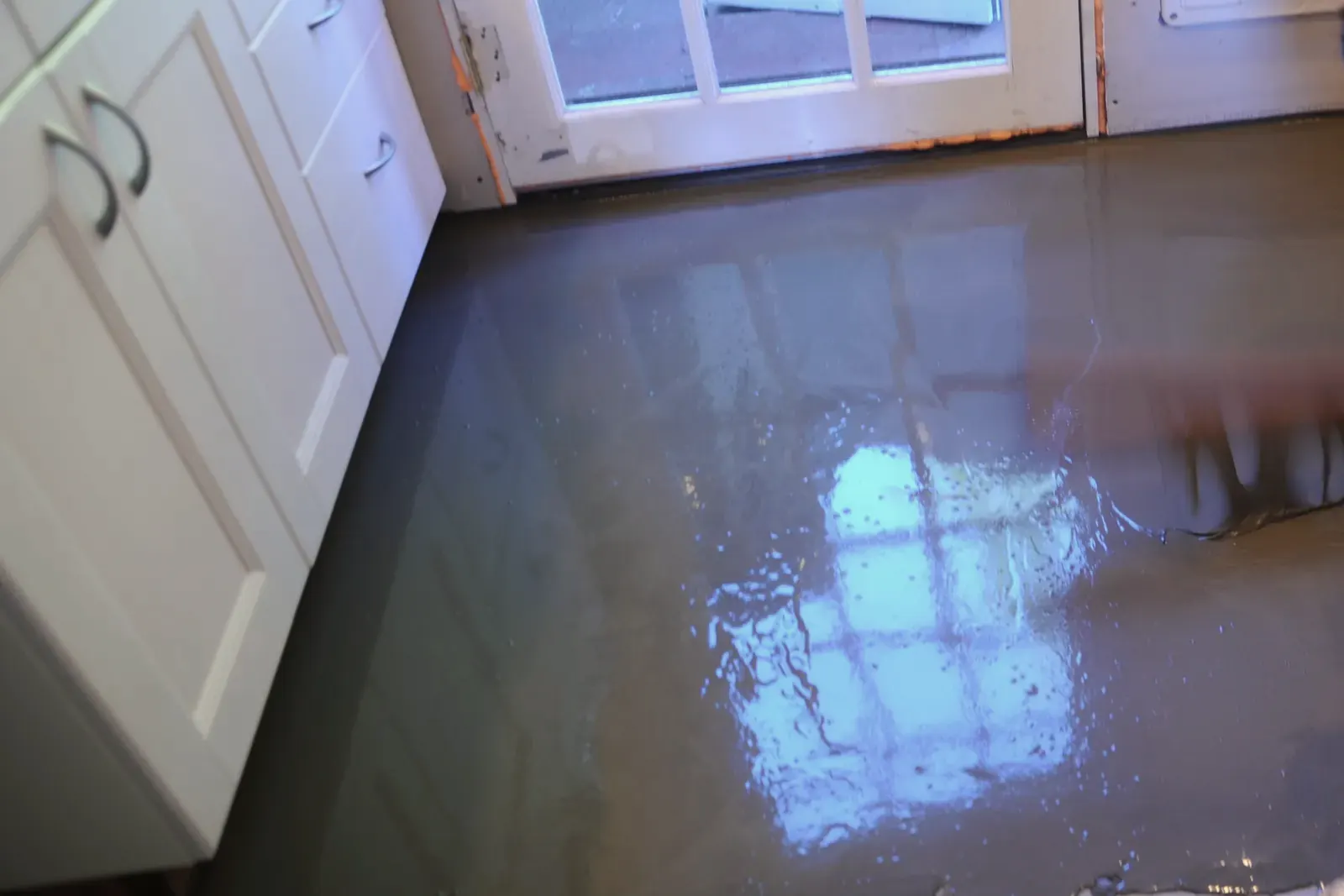 Freshly poured self-leveling underlayment over a kitchen floor, the window of the door reflected in the wet surface
