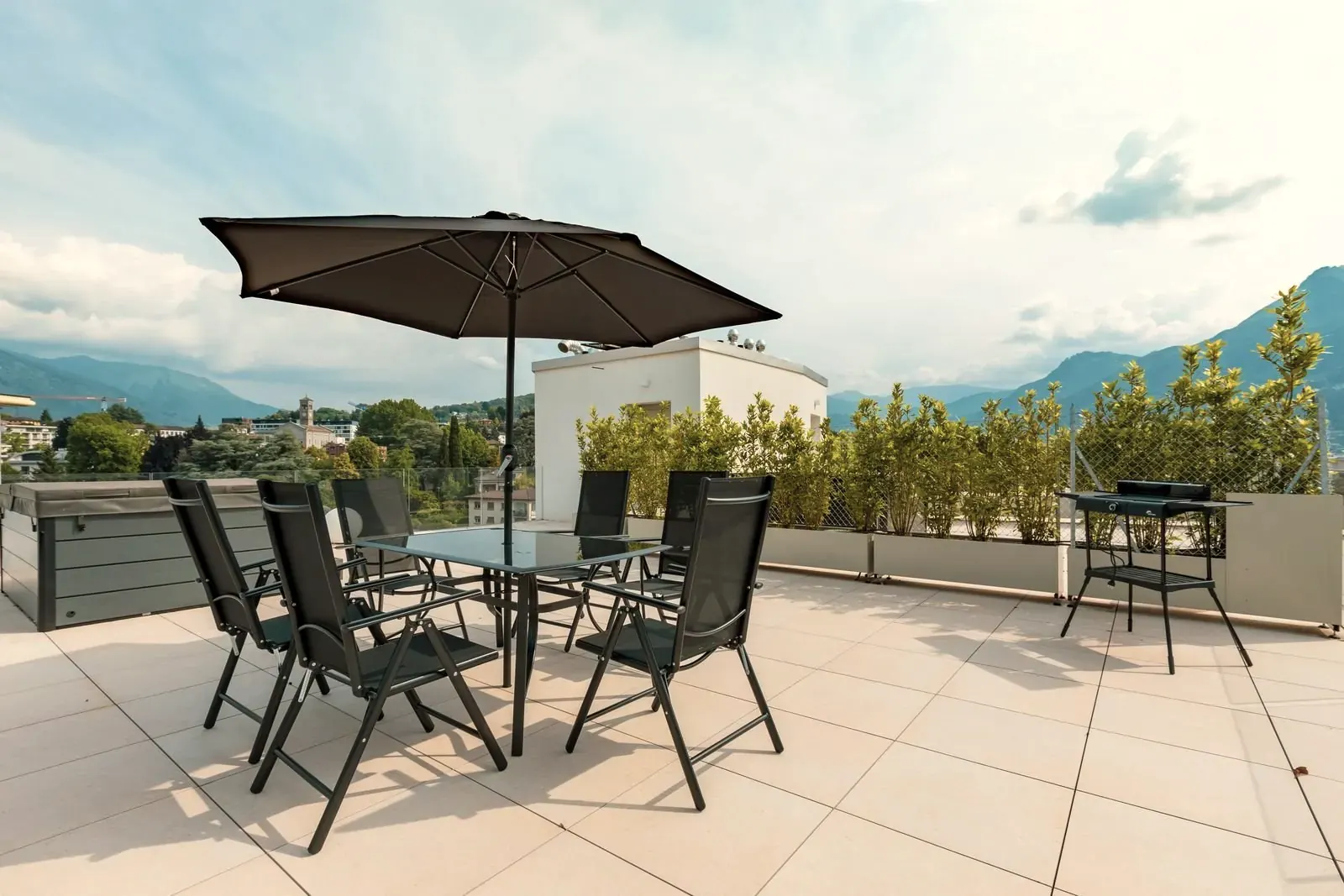 Roof terrace laid with large light porcelain slabs, with a table, chairs and parasol