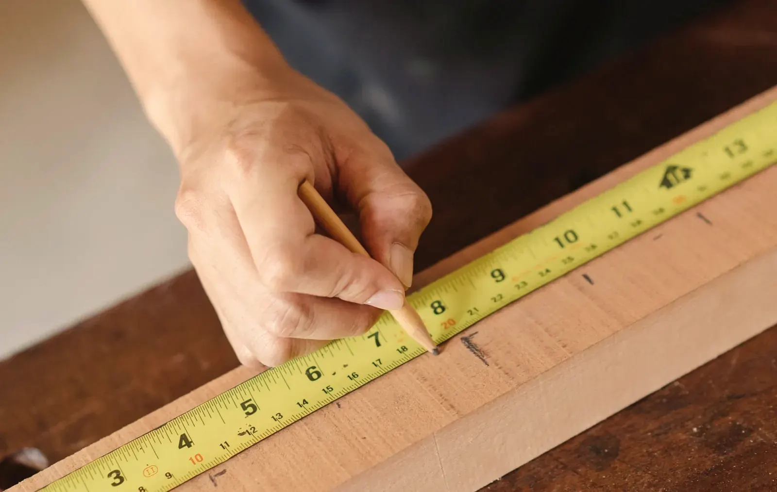 Hand marking a cut on a wooden board with a pencil and a tape measure