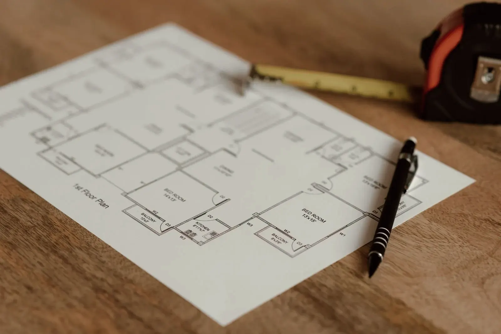 Printed floor plan on a wooden table with a pen and a tape measure