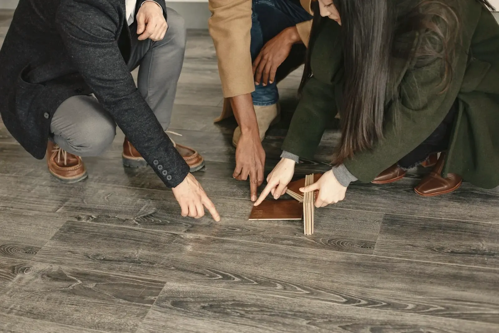 Three people crouching on a laid plank floor, pointing at flooring samples